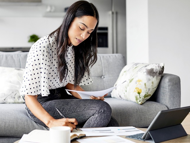 Woman at home with laptop in front of her, looking at papers